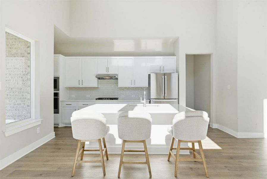 Kitchen featuring white cabinetry, a towering ceiling, a kitchen breakfast bar, a center island with sink, and appliances with stainless steel finishes