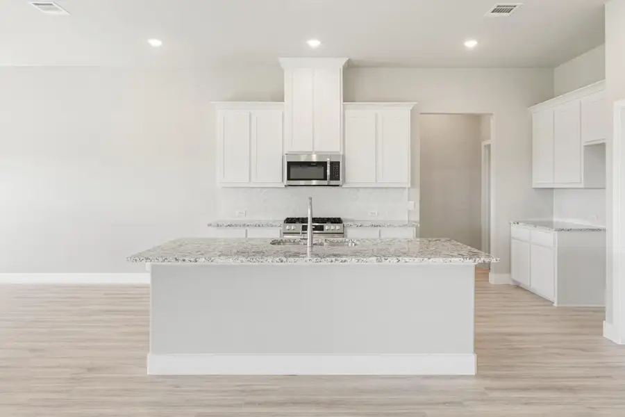 Kitchen with large center island, granite countertops, white cabinets, and stainless steel appliances