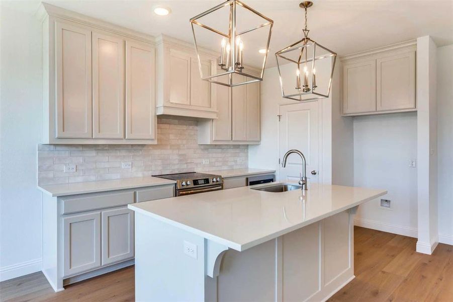 Kitchen with tasteful backsplash, light wood finished floors, decorative light fixtures, an island with sink, and recessed lighting