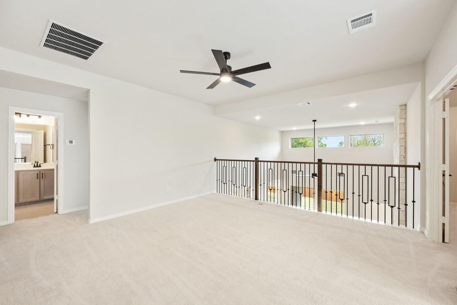Open upstairs loft with carpet flooring, ceiling fan, and iron railing overlooking lower level