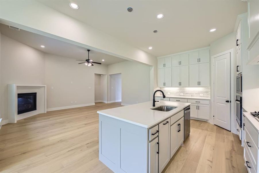 Kitchen featuring light wood finished floors, tasteful backsplash, stainless steel appliances, an island with sink, and ceiling fan Kitchen featuring light wood finished floors, tasteful backsplash, stainless steel appliances, an island with sink, and ceiling fan