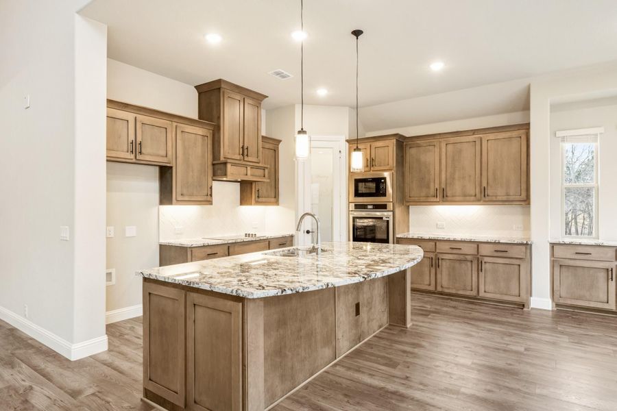 Kitchen with large granite island, brown wood cabinets, stainless steel appliances, and hardwood floors Kitchen with large granite island, brown wood cabinets, stainless steel appliances, and hardwood floors