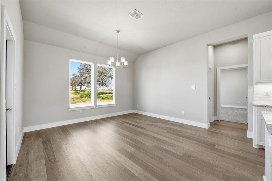Unfurnished dining area with a chandelier, vaulted ceiling, and light wood-style floors