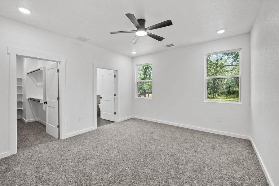 A well-lit bedroom features plush carpeting, a modern ceiling fan, and ample storage within the walk-in closet. A well-lit bedroom features plush carpeting, a modern ceiling fan, and ample storage within the walk-in closet.