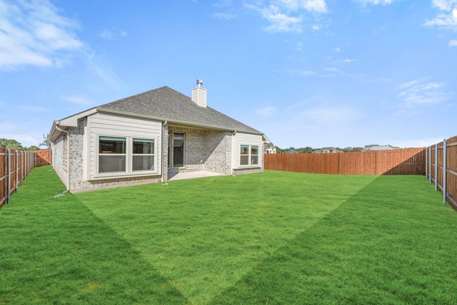 Rear exterior of single-story brick home with large fenced backyard and green lawn