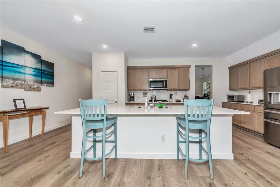 Kitchen with decorative backsplash, a kitchen island with sink, light wood-type flooring, refrigerator with ice dispenser, and sink