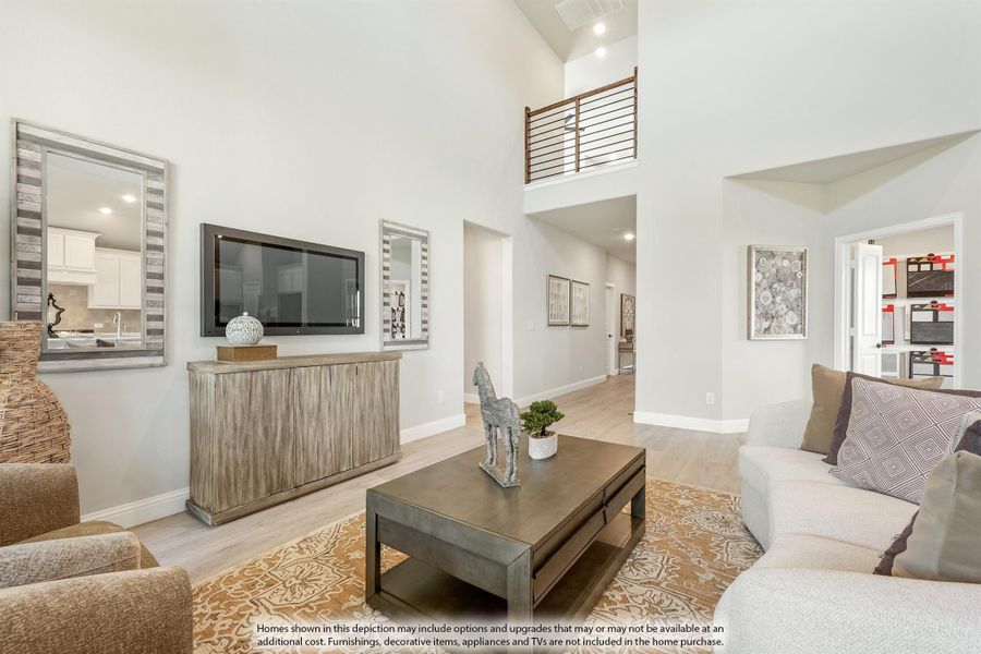 Open living room with two-story ceiling, wood floors, wall-mounted TV, and second-floor overlook railing. Open living room with two-story ceiling, wood floors, wall-mounted TV, and second-floor overlook railing.