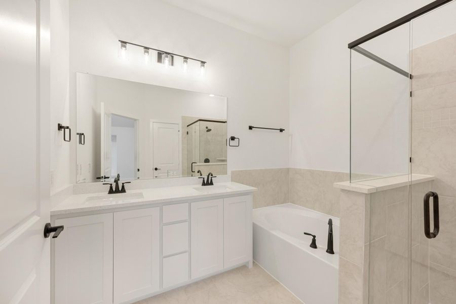 Bathroom with double vanity, soaking tub, and glass-enclosed shower with tile surround and black fixtures Bathroom with double vanity, soaking tub, and glass-enclosed shower with tile surround and black fixtures