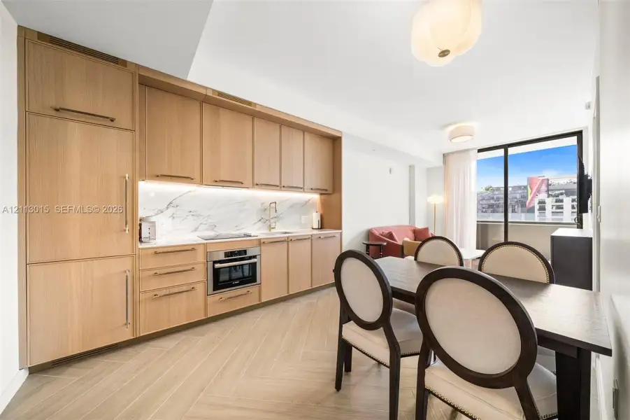 Kitchen featuring light wood-finish cabinetry, integrated refrigerator, stone-style backsplash, built-in wall oven, and herringbone-patterned flooring