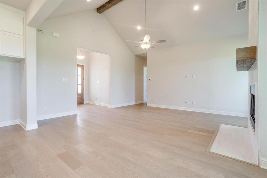 Unfurnished living room with beam ceiling, ceiling fan, high vaulted ceiling, and light wood-type flooring