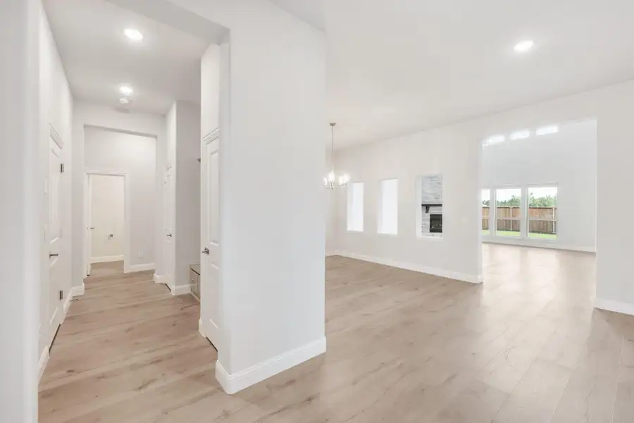 Open living area with light wood floors, white walls, chandelier, fireplace, and hallway leading to bedrooms