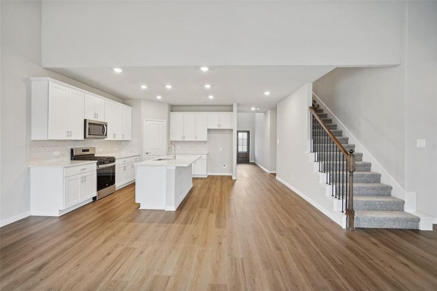 Kitchen with stainless steel appliances, light hardwood / wood-style flooring, and an island with sink