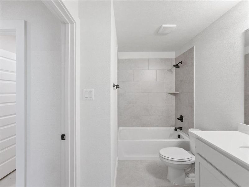 Modern bathroom featuring a white porcelain tub, matte black fixtures, light gray tile surround, built-in shower shelf, and a white vanity with an integrated sink Modern bathroom featuring a white porcelain tub, matte black fixtures, light gray tile surround, built-in shower shelf, and a white vanity with an integrated sink