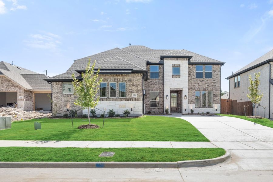 Two-story brick and stone home with dark roof, front lawn, and concrete driveway in a new subdivision Two-story brick and stone home with dark roof, front lawn, and concrete driveway in a new subdivision