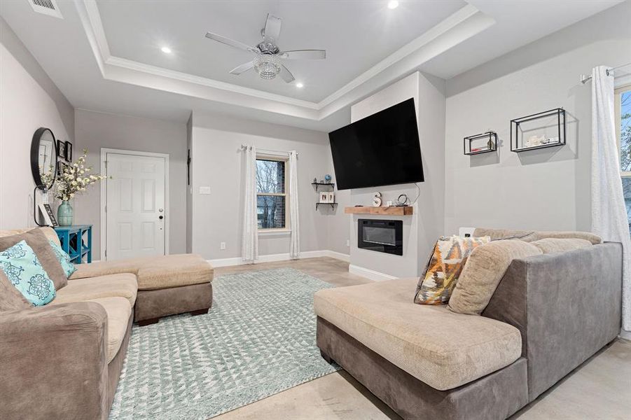 Living room featuring ceiling fan, ornamental molding, a raised ceiling, and a wealth of natural light