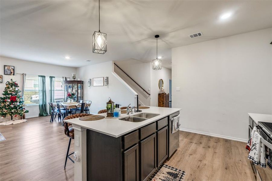 Kitchen with light wood-style floors, dark brown cabinets, hanging light fixtures, stainless steel appliances, and a kitchen island with sink Kitchen with light wood-style floors, dark brown cabinets, hanging light fixtures, stainless steel appliances, and a kitchen island with sink
