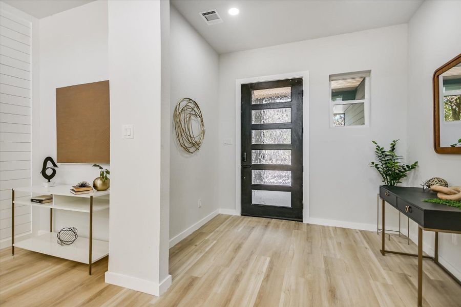 Step into a light-filled entry with warm wood flooring and a modern glass-paneled front door.
