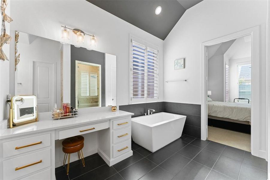 This bathroom features a contemporary freestanding bathtub, a vanity with ample storage and a large mirror, and tiled flooring