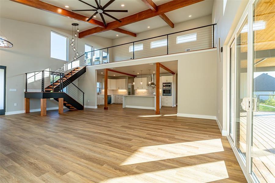 Unfurnished living room with beamed ceiling, stairway, light wood finished floors, recessed lighting, and a high ceiling Unfurnished living room with beamed ceiling, stairway, light wood finished floors, recessed lighting, and a high ceiling
