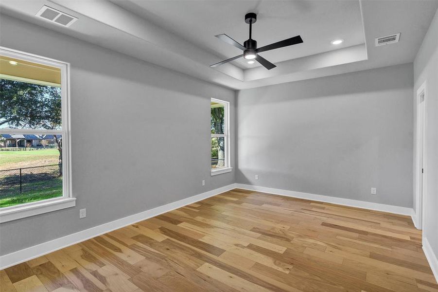 Empty room with light wood-style flooring, a tray ceiling, recessed lighting, and ceiling fan