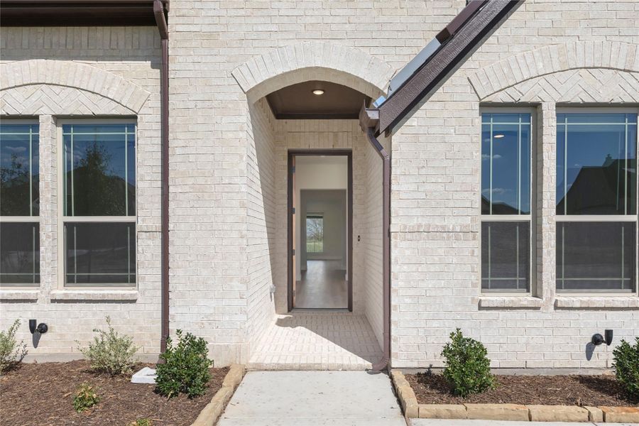Home entrance with arched brick surround, open front door, and concrete walkway leading inside.