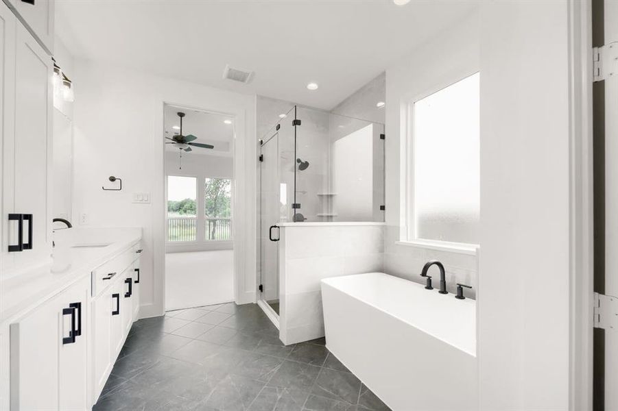 Spacious bathroom featuring a freestanding soaking tub with matte black fixtures, a walk-in shower with glass enclosure, dual vanity with white cabinetry and dark hardware, and dark tile flooring