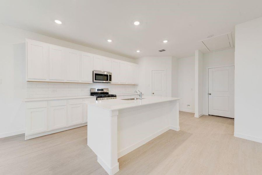 Kitchen featuring backsplash, an island with sink, appliances with stainless steel finishes, white cabinetry, and recessed lighting Kitchen featuring backsplash, an island with sink, appliances with stainless steel finishes, white cabinetry, and recessed lighting