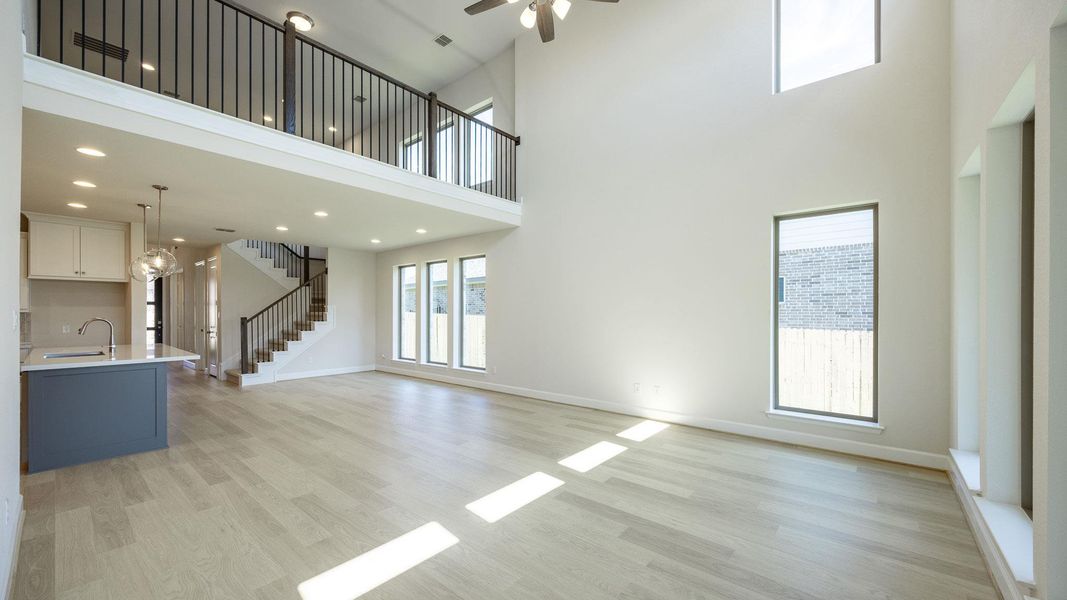 Unfurnished living room with light wood finished floors, a towering ceiling, stairway, ceiling fan, and recessed lighting