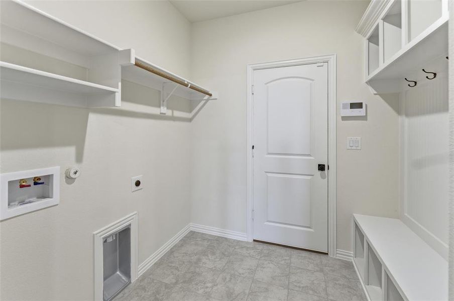 Utility room featuring grey tile flooring, built-in shelving, a clothes hanging rod, and a built-in bench with storage cubbies