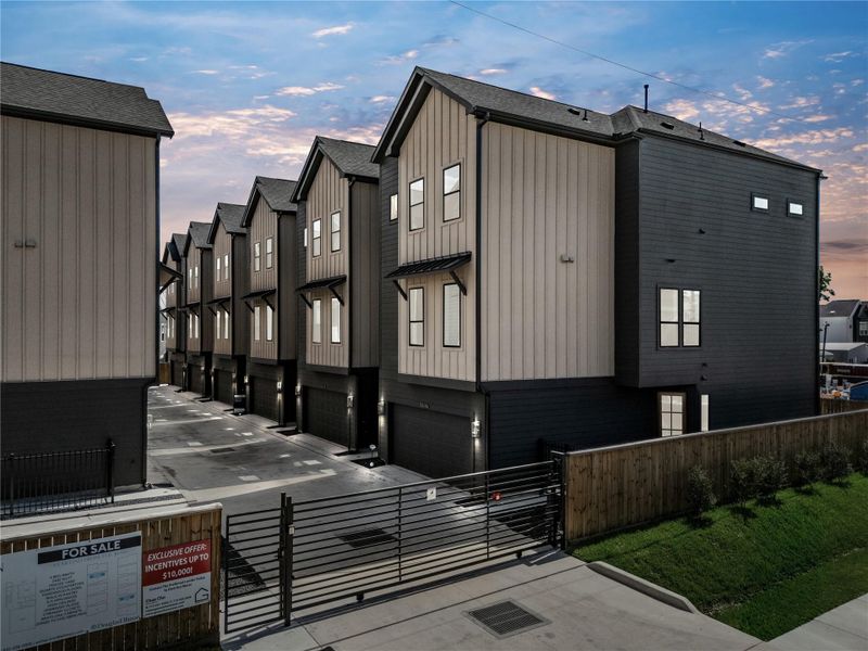 Modern three-story single family homes with a sleek design, featuring two-tone exteriors and attached garages. The homes are situated along a clean, paved driveway, with a fenced area providing added privacy. Modern three-story single family homes with a sleek design, featuring two-tone exteriors and attached garages. The homes are situated along a clean, paved driveway, with a fenced area providing added privacy.