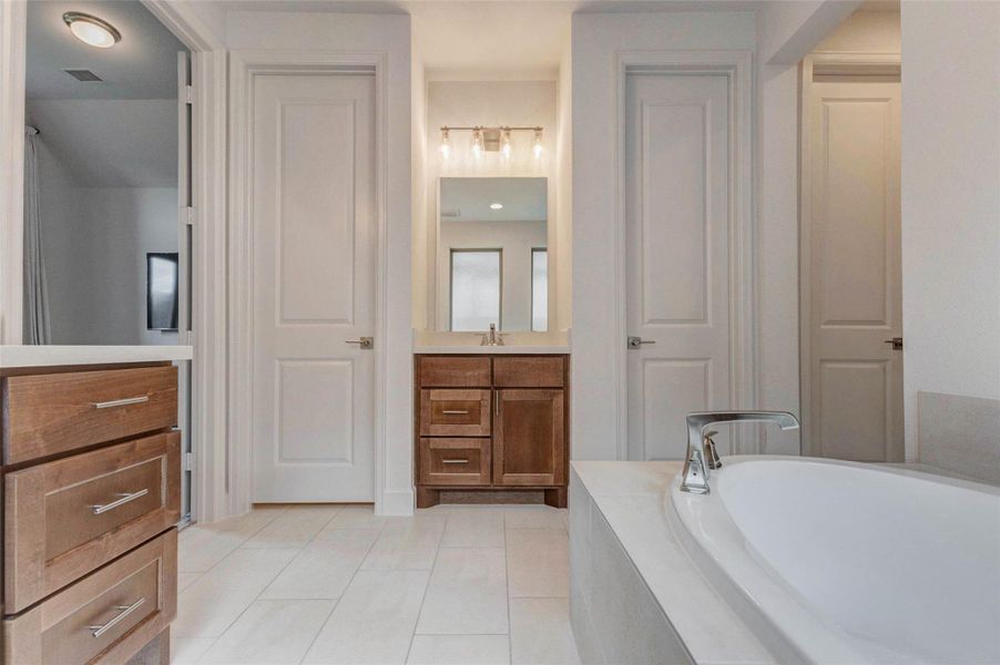 This bathroom features a modern design with a large soaking tub, double doors, sleek wooden cabinetry, and a well-lit vanity area. Neutral tones and clean lines create a serene atmosphere. This bathroom features a modern design with a large soaking tub, double doors, sleek wooden cabinetry, and a well-lit vanity area. Neutral tones and clean lines create a serene atmosphere.