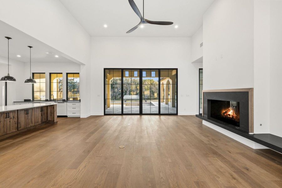 Unfurnished living room featuring dark wood-style flooring, a warm lit fireplace, a ceiling fan, a high ceiling, and recessed lighting