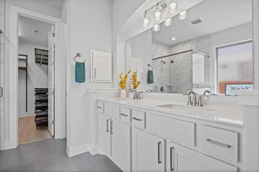 A well-lit primary bathroom features a dual vanity, sleek shower, and an adjacent walk-in closet.
