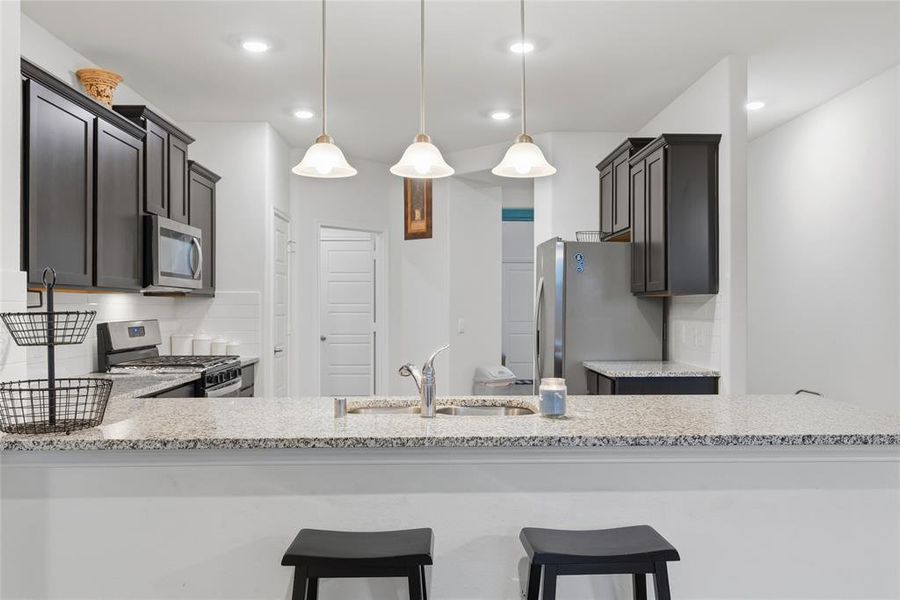 Kitchen featuring a granite countertop island with a stainless steel sink, pendant lighting, dark wood-finish cabinetry, stainless steel appliances, and a white subway tile backsplash