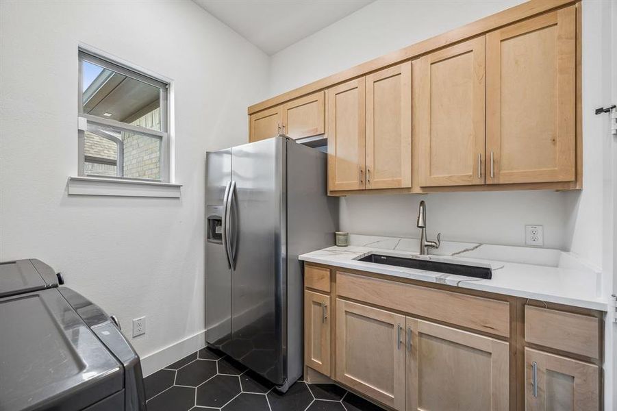 Kitchen with light wood finish cabinetry, stainless steel fridge with ice dispenser, dark tile patterned flooring, and washing machine and dryer