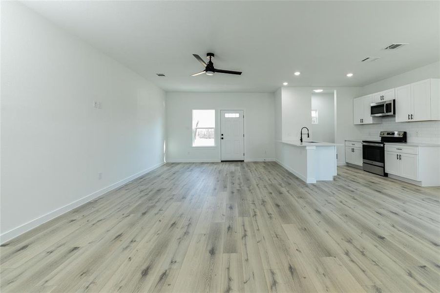 Unfurnished living room with ceiling fan, light wood-type flooring, and sink