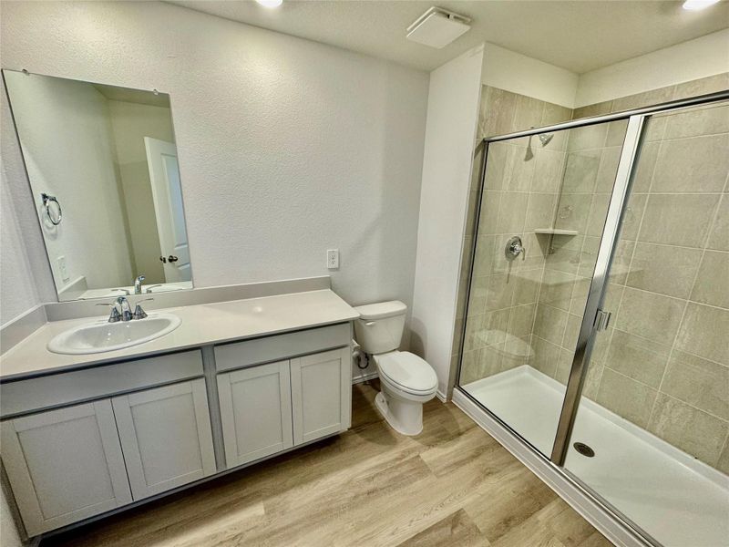 Bathroom with light wood-style flooring, vanity, a textured wall, and a shower stall
