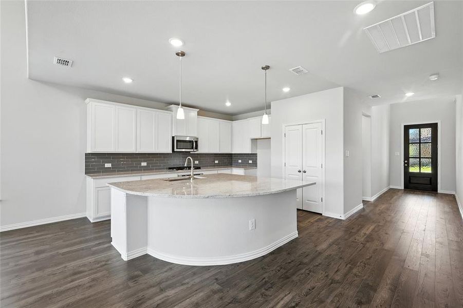 Kitchen with a center island with sink, white cabinetry, dark wood-style flooring, light stone counters, and hanging light fixtures