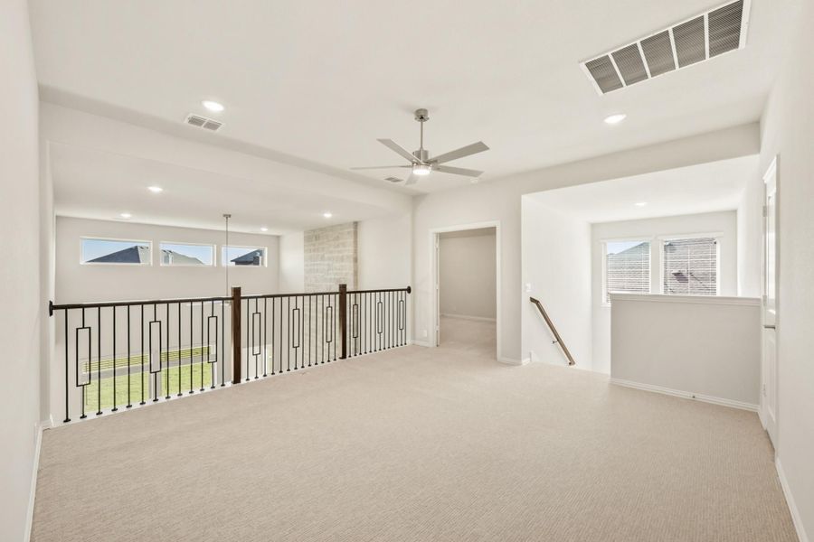 Open upstairs loft with carpet, ceiling fan, and iron railing overlooking lower level