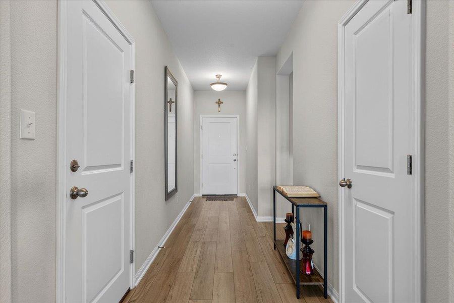Smooth wood-look flooring guides visitors through a welcoming long hallway lined with classic paneled interior doors.