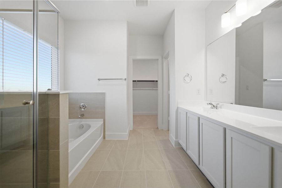 Full bath featuring double vanity, a spacious closet, a bath, a shower stall, and light tile patterned flooring