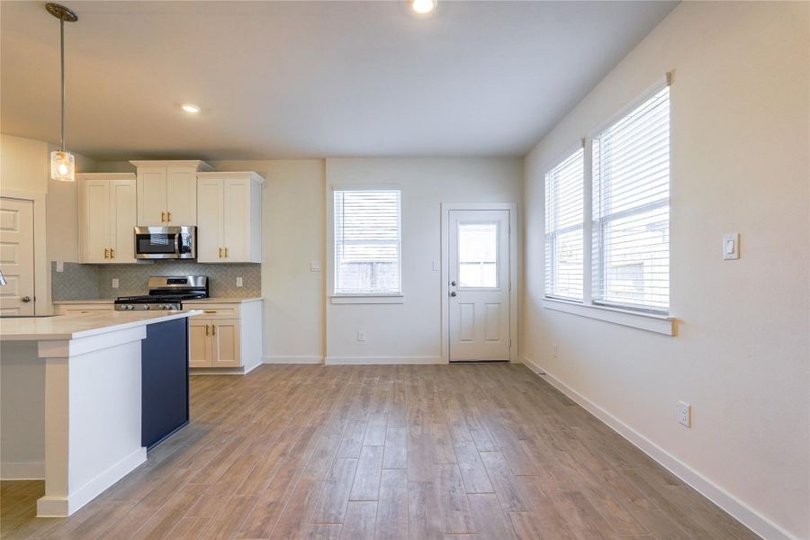 This photo showcases a bright, open kitchen and dining area featuring modern white cabinetry, a gas stove, and hardwood floors. Large windows provide ample natural light, and there's a door leading outside, adding convenience and charm.