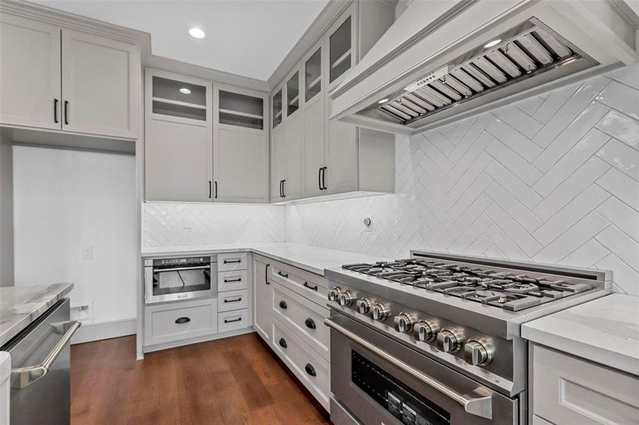 Kitchen featuring appliances with stainless steel finishes, tasteful backsplash, light stone countertops, custom range hood, and dark hardwood / wood-style flooring