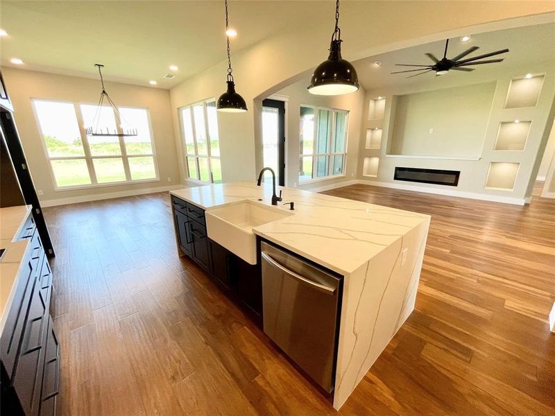 Kitchen featuring hardwood / wood-style floors, sink, dishwasher, pendant lighting, and a center island with sink