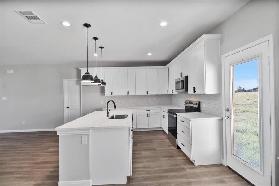 Kitchen with decorative light fixtures, a healthy amount of sunlight, a kitchen island with sink, and appliances with stainless steel finishes