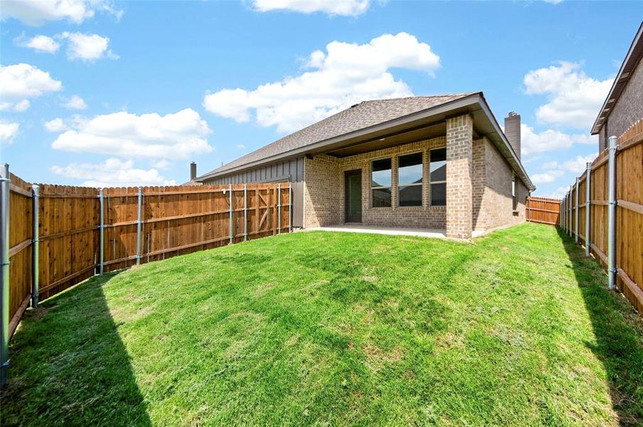 Expansive backyard featuring a manicured lawn, full privacy fencing, and a covered patio
