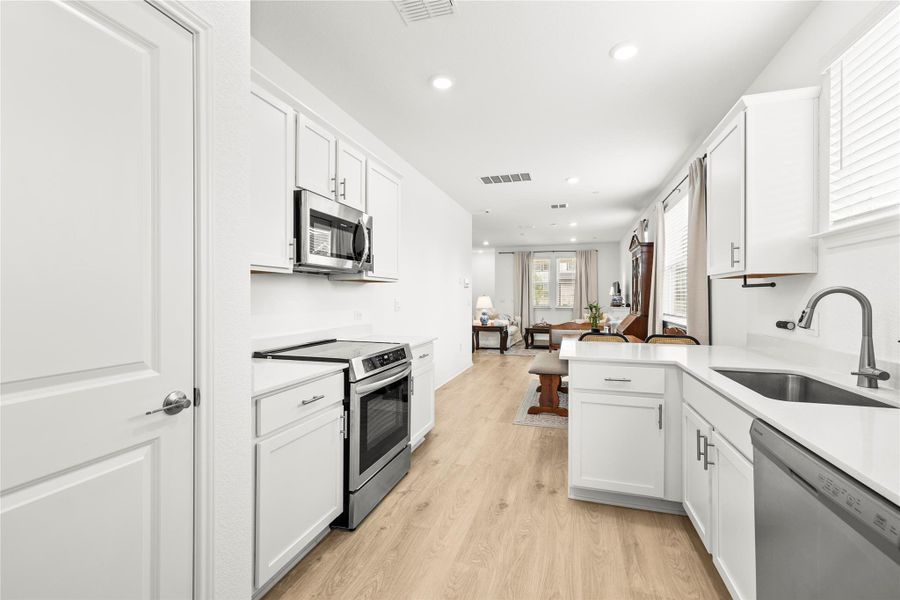 A well-lit kitchen with sleek white cabinetry transitions seamlessly into a comfortable living space.