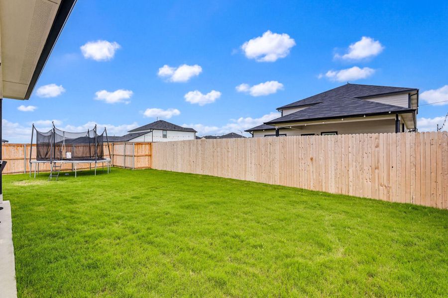 Expansive backyard featuring a manicured lawn, full wood privacy fencing, and a concrete patio extending from the home