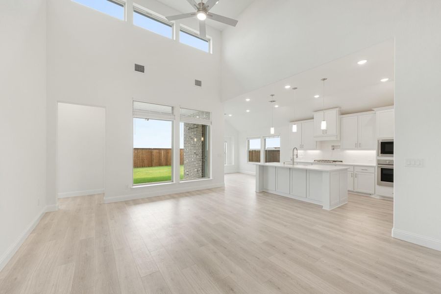 Open-concept living area with high ceilings, light wood floors, and white kitchen island with pendant lights
