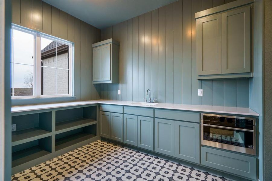 Kitchen featuring sink, wooden walls, gray cabinetry, and stainless steel oven